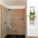 Douche à l'italienne avec verre, carrelage beige, étagère et plantes