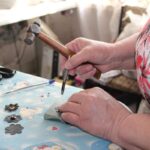 Une personne martèle un clou sur une table recouverte de motifs floraux, entourée d'outils de bricolage