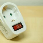 Adaptateur électrique blanc avec interrupteur rouge sur plan de bois