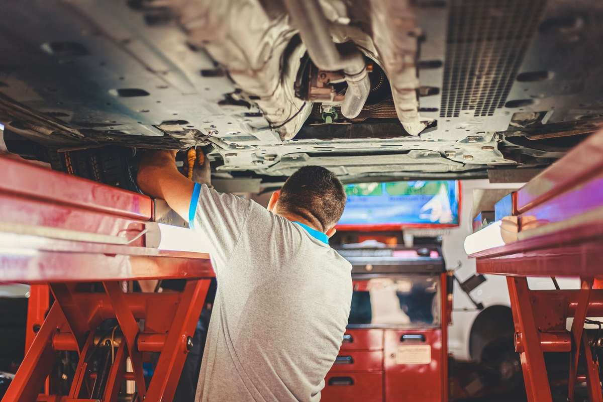 Mécanicien inspectant le dessous d'un véhicule soulevé dans un garage équipé Mécanicien inspectant le dessous d'un véhicule soulevé dans un garage équipé