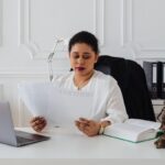 Femme lit des documents dans un bureau avec un ordinateur portable et une statue